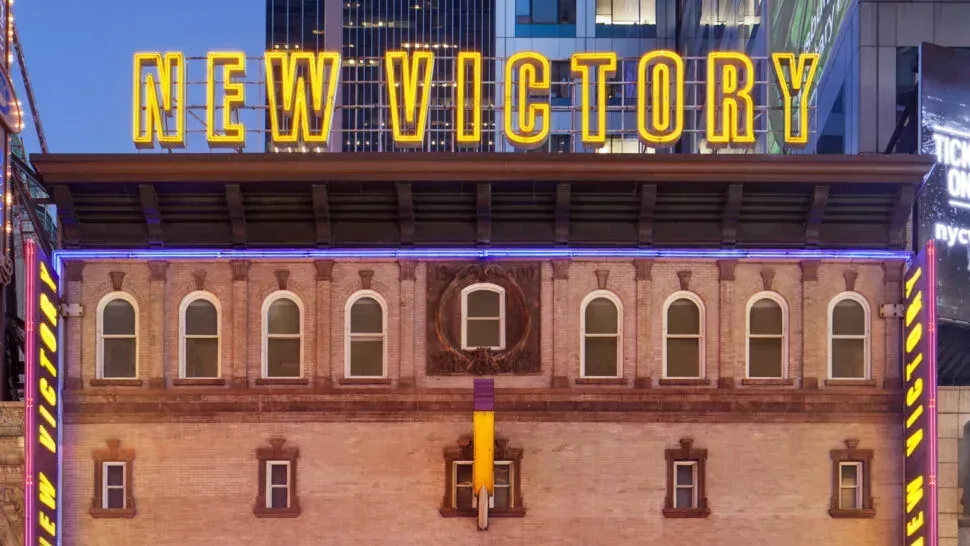 The New Victory Theater facade on 42nd Street with the marquee lit in yellow.